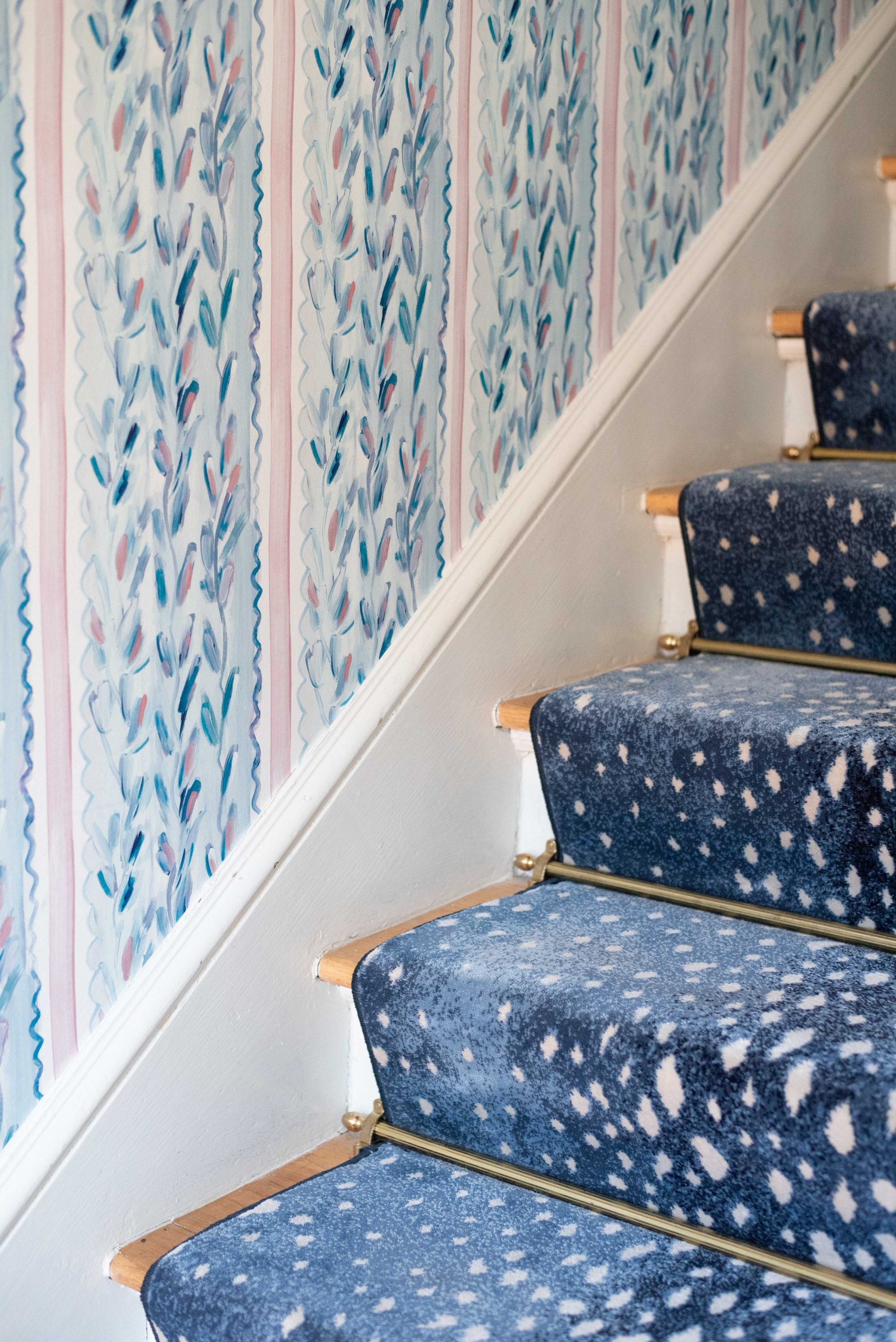 Blue and pink striped wallpaper and stairs with blue carpet and brass rods